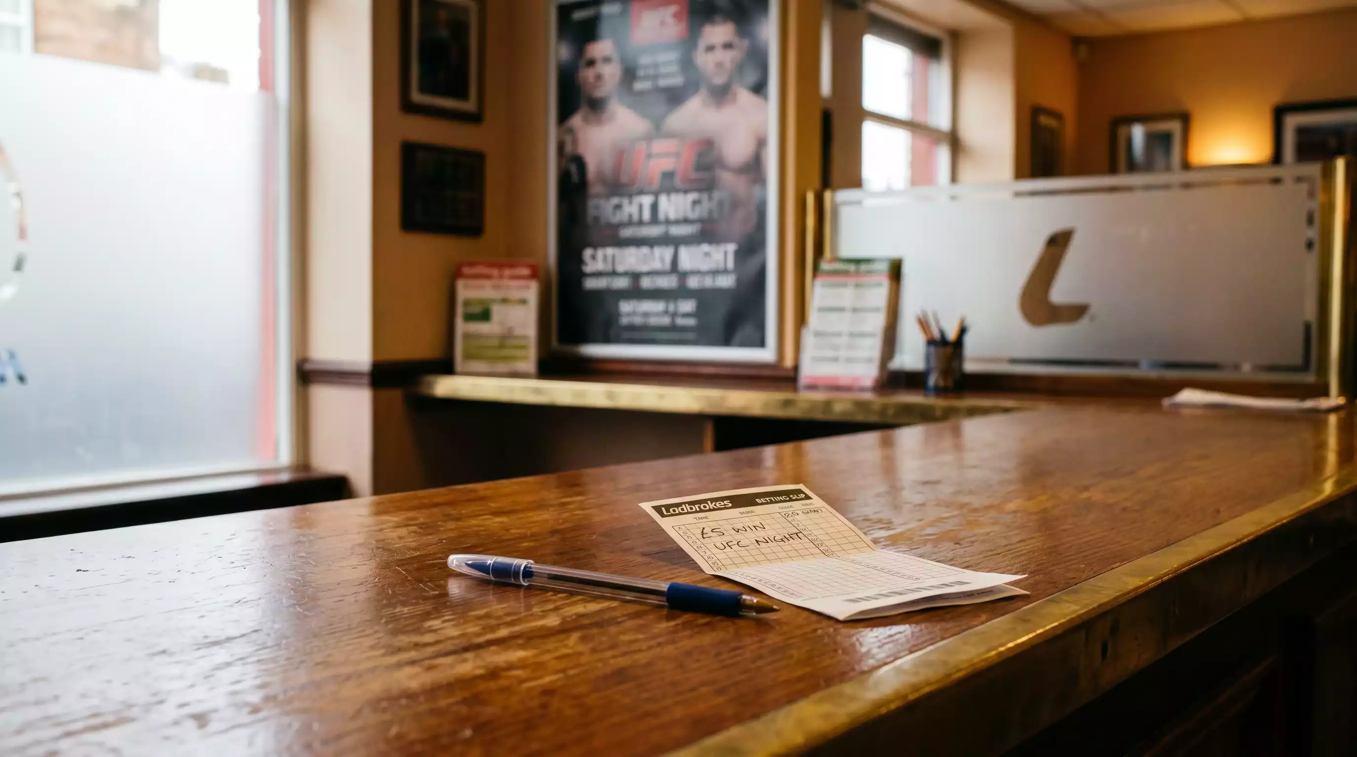 Wooden counter of a British high-street betting shop with a fight card poster behind